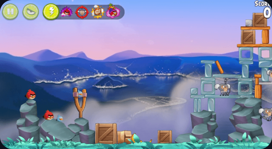 Angry Birds: red birds beside a slingshot on the rocks, facing a tower of wood and glass blocks across a misty bay