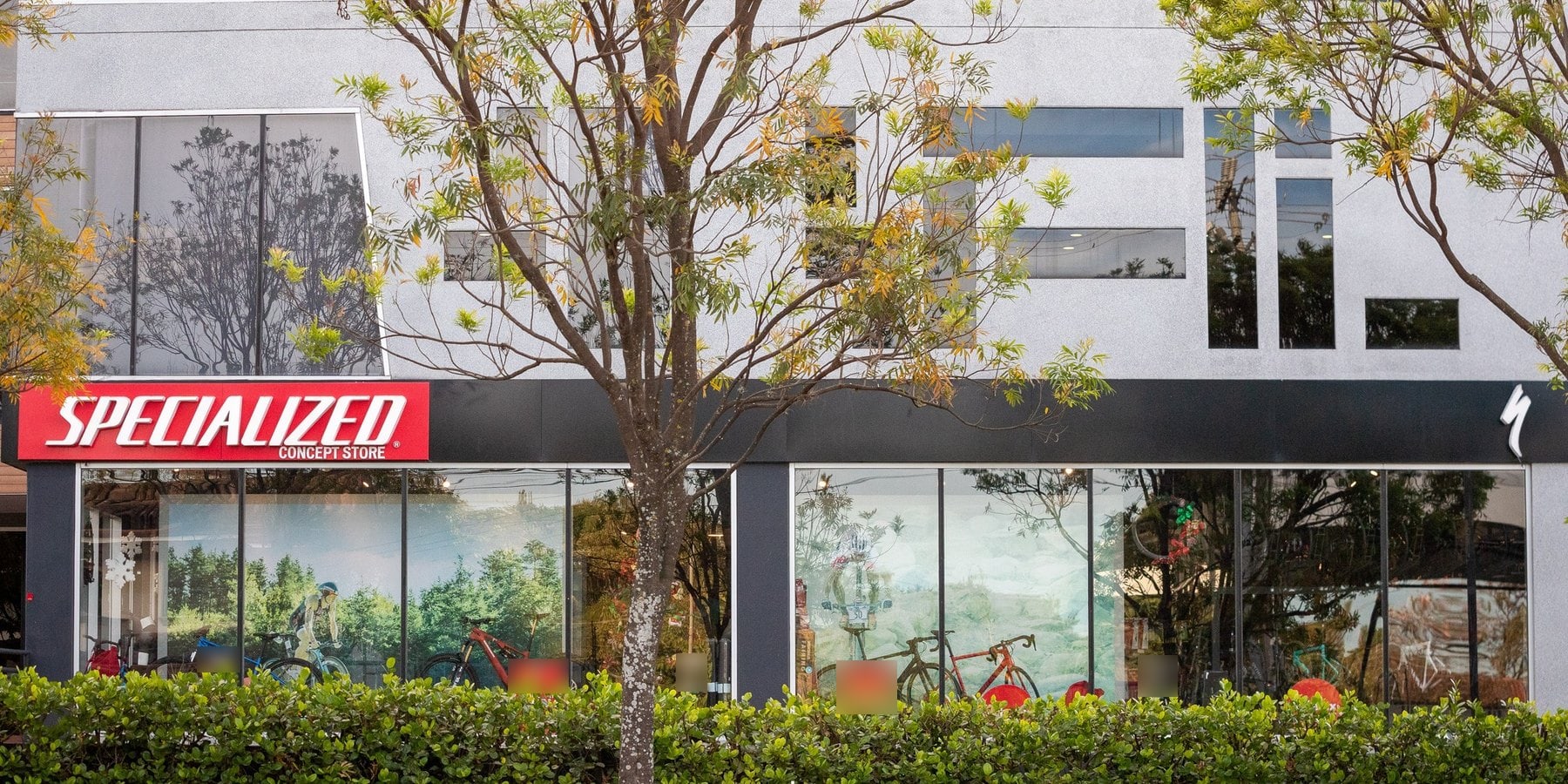 Front of a Specialized concept store in Costa Rica: a red Specialized sign over a glass shopfront with bikes inside, trees and a hedge in front